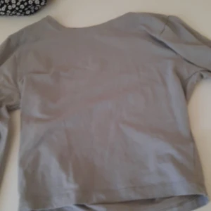 Ljusgrå långärmad tröja - En enkel och stilren ljusgrå långärmad tröja i mjukt material. Perfekt att matcha med jeans eller kjol för en avslappnad look. Rund halsringning och rak passform.