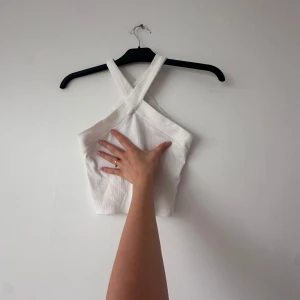 Vit croppad linnetopp med korsade axelband - Säljer en vit croppad linnetopp med breda korsade axelband. Toppen har en stilren och modern design som passar perfekt till sommaren. Materialet känns svalt och bekvämt.