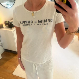 Vit t-shirt från Ralph Lauren - Vit t-shirt från Ralph Lauren med svart text 'DENIM & SUPPLY' tryckt på bröstet. Klassisk rund halsringning och korta ärmar. 
