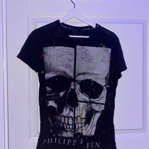 Svart t-shirt  från Philipp Plein äkta  - Cool svart t-shirt från Philipp Plein med stor dödskalle-tryck framtill och färgstänk i grönt, gult och rött. Klassisk passform och rund halsringning. Perfekt för dig som gillar edgy streetstyle. STORLEK S köpt 2021 använd i ca 9 månader annars bara hängt i garderoben !PRIS KAN DISKUTERAS! INGA SKADOR KÖPT FÖR UNGEFÄR 1500 kr 