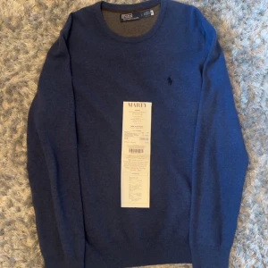 Blå ulltröja från Polo Ralph Lauren - Mörkblå tröja från Polo Ralph Lauren i mjuk ullblandning. Klassisk rund halsringning och diskret broderad logga på bröstet. Perfekt för en stilren och enkel look.