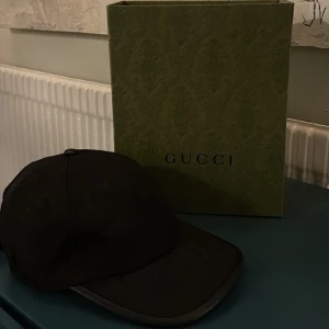 Svart keps från Gucci - Snygg svart keps från Gucci med diskret GG-mönster. Kepsen har böjd skärm och justerbart spänne baktill för perfekt passform. Klassisk och stilren design med märkets logga invävd i tyget.