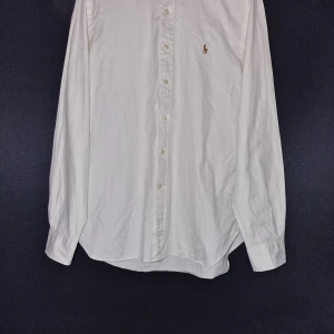 Vit skjorta från Polo Ralph Lauren - Klassisk vit skjorta från Polo Ralph Lauren i slim fit-modell. Skjortan har långa ärmar, knappar framtill och en liten broderad logga på bröstet. Perfekt för en stilren och clean look. Passar som en large då den är slim fit