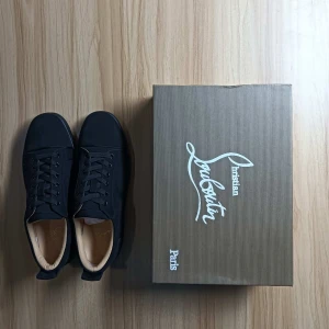 Svarta sneakers från Christian Louboutin - Säljer ett par svarta sneakers från Christian Louboutin med klassisk röd sula. Skorna har snörning, rund tå och är tillverkade i mocka. Diskret broderad logga på hälen och stilren design.