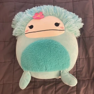 Stor Squishmallows plyschleksak blå axolotl - Supermjuk och stor Squishmallows plyschleksak i form av en blå axolotl med fluffig man, glittriga tassar och en rosa blomma på huvudet. Perfekt som kramkompis eller dekoration i sängen.