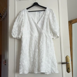 Vit blommig klänning från Bubbleroom - Superfin vit klänning från Bubbleroom med 3D-blommönster, v-ringning och puffärmar. Klänningen har omlottkänsla framtill och är kort i modellen. Perfekt för sommarens tillfällen! Nypris 899kr