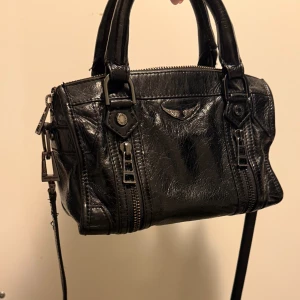 Svart handväska från Zadig & Voltaire - Säljer en svart handväska från Zadig & Voltaire i skinn med dubbla handtag och avtagbar axelrem. Väskan har silverfärgade metalldetaljer, dragkedja upptill och dekorativa dragkedjor framtill. Perfekt storlek. Nypris 5000 kr 