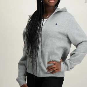 Grå hoodie från Ralph Lauren - Säljer en klassisk grå hoodie från Ralph Lauren med dragkedja och fickor framtill. Tröjan har en liten broderad logga på bröstet och är perfekt för en avslappnad stil. Mjuk och bekväm med långa ärmar och huva.