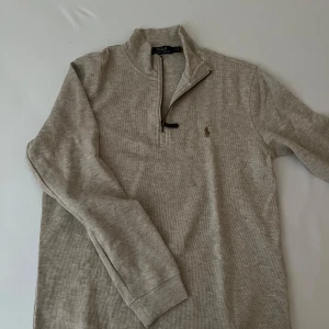 Beige långärmad tröja med dragkedja från Polo Ralph Lauren - Säljer en beige långärmad tröja från Polo Ralph Lauren med halv dragkedja och broderad logga på bröstet. Tröjan är i mjuk bomull och har ribbade muddar vid ärmslut och nederkant. Perfekt för lager-på-lager-stil.