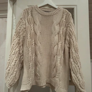 Beige stickad tröja med flätmönster från Vero Moda - Säljer en beige stickad tröja från Vero Moda med snyggt flätmönster framtill och på ärmarna. Tröjan har rund halsringning och långa ärmar med breda muddar. 