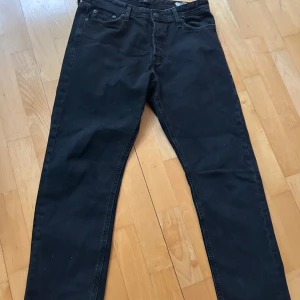 Svarta jeansbyxor - Säljer ett par svarta jeansbyxor från Jack & Jones med klassisk femficksdesign och raka ben. Byxorna har normal passform och stängs med dragkedja och knapp. Perfekta till vardags och enkla att matcha med olika stilar. Storlek w31/L32
