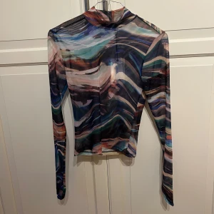 Mönstrad mesh polotopp från Bik Bok - Säljer en tunn och transparent mesh polotopp från Bik Bok i storlek XS. Toppen har ett färgstarkt abstrakt mönster i blått, grönt, lila, beige och svart samt långa ärmar och hög hals. Är oanvänd. 
