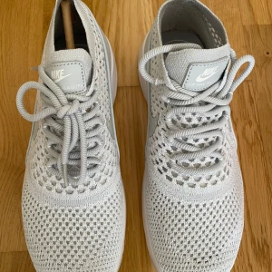 Nike Air Max Thea Ultra FK i ljusgrått - Nike Air Max Thea Ultra FK sneakers i ljusgrått med stickad ovandel och vit sula. Skorna har snörning och en luftig, stickad design som ger en modern look. Perfekta för dig som gillar stilrena och bekväma sneakers.