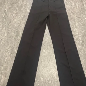 Svarta kostymbyxor från Kappahl - Säljer ett par klassiska svarta kostymbyxor från Kappahl. Byxorna har raka ben, hög midja och stängs med dragkedja och hake. Perfekta för en stilren look och passar till många olika tillfällen.