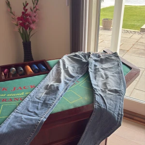 Ljusblå jeansbyxor från tramarossa - Säljer ett par ljusblå jeansbyxor från tramarossa med klassisk fyraficksdesign och röda detaljer på bakfickorna. Byxorna har normal passform och är perfekta för en avslappnad stil. Dragkedja och knapp framtill. Size 32 