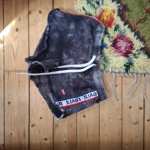 Svarta shorts från Levi's med snörning - Säljer ett par svarta shorts från Levi's med batikmönster och vit snörning i midjan. Shortsen har en tydlig Levi's-logga längs kanten och är perfekta för avslappnade dagar.