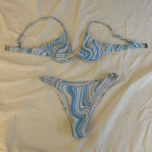Blåvit mönstrad bikini från SHEIN - Säljer en bikini från SHEIN i storlek S med blått och vitt vågigt mönster. Bikinin har bygel-bh med justerbara axelband och matchande trosa med hög benskärning. Perfekt för stranden eller poolen!