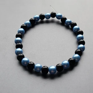 Svart och blått pärlarmband - Säljer ett stilrent armband med pärlor i svart och metallicblå färg. Armbandet är elastiskt och passar de flesta handleder. Perfekt accessoar för att addera lite färg till din outfit.
