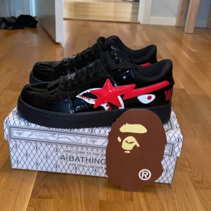  Bape  sneakers  - Säljer ett par svarta Bape Sta sneakers i lackad syntet med röd stjärndetalj och hajmönster på sidan. Skorna har snörning, rund tå och platt sula. Kommer med originalkartong och Bape-tag. Pris kan diskuteras!