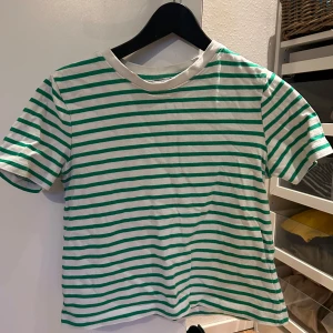 Randig t-shirt från Zara - Säljer en vit t-shirt med gröna ränder från Zara. T-shirten har korta ärmar och rund halsringning med vit kant. Perfekt för en avslappnad stil och passar till det mesta. Superenkel att matcha med jeans eller shorts!