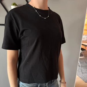 Svart croppad t-shirt - En enkel svart croppad t-shirt med rund halsringning. T-shirten har korta ärmar och är tillverkad i ett mjukt bomullsmaterial. Perfekt till jeans eller shorts för en avslappnad stil.