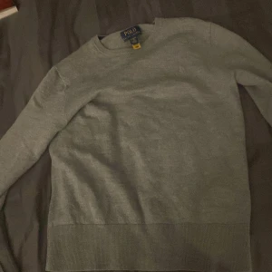 Grå stickad tröja från Polo Ralph Lauren - Säljer en klassisk grå stickad tröja från Polo Ralph Lauren med rund halsringning och diskret broderad logga på bröstet. Perfekt för en stilren och enkel look. Tröjan har långa ärmar och ribbade muddar. Vet inte exakt vilken storlek den är men den passar xs, säljer den för att de har blivit för liten. Skriv till mig för frågor eller bud. Pris kan diskuteras 😃