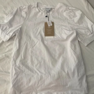 Vit kortärmad topp från Aware - säljer en heltny vit topp från aware med prislappen kvar. den har korta ärmar och lätt puff vid axlarna. toppen har en rund halsringning och är gjord i mjuk bomull 🫶🏻kommer självklart stryka tröjan innan jag skickar iväg den!