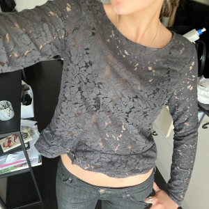 Mörkgrå spetsblus med lång ärm - Säljer en mörkgrå, transparent spetsblus med lång ärm. Blusen har ett blommigt spetsmönster och rund halsringning. Perfekt för dig som gillar en stilren men ändå detaljrik look.