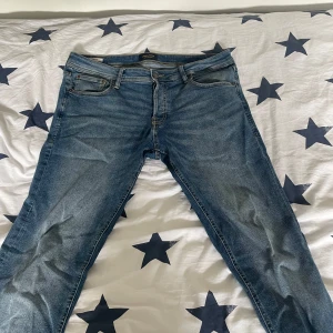 Jack and Jones jeans  - Klassiska blå jeans från Jack and Jones med fem fickor och dragkedja. Byxorna har en rak passform och subtila slitningar framtill. Perfekta till vardags.
