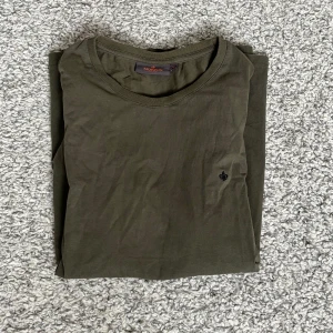 Olivgrön t-shirt från Morris - Säljer en stilren olivgrön t-shirt från Morris. T-shirten har rund halsringning, korta ärmar och en liten broderad logga på bröstet. Perfekt till jeans eller shorts för en avslappnad look.