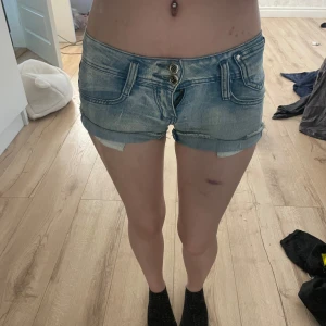 Blå lågmidjade jeansshorts - Säljer ett par ljusblå jeansshorts med dubbla knappar framtill. Storlek står inte men skulle gissa på att det är xs. Säljer för att dom kommer inte till använda och börjar bli försmå. Gylfen fungerar men är trög och på bilden har jag inte dragit upp den efftersom dom är försmå så jag får inte upp den. Pris går att diskutera 