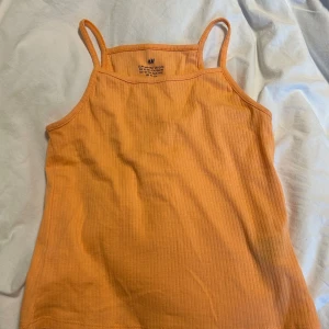 Ribbad orange linnetopp från H&M - Säljer en ribbad orange linnetopp från H&M med smala axelband. Perfekt för varma dagar och enkel att matcha med jeans eller shorts.