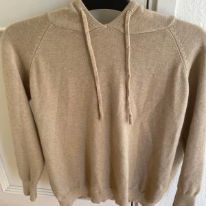 Merinoull hoodie - En fin, stilig merinoull hoodie i beige färg. Den är i gott skick och är använd ett fåtal gånger. Passar perfekt både till ett par shorts på sommaren eller antingen till en kallare dag med ett par jeans.