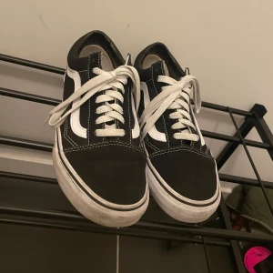 Svarta Vans  - Klassiska Vans i svart med vit sula och vit sidorand. Skorna har snörning. Perfekta för en avslappnad och stilren look.