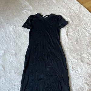 Svart t-shirtklänning från H&M - En enkel svart t-shirtklänning från H&M i storlek XS. Klänningen har rund halsringning och korta ärmar, tillverkad i mjukt material som känns bekvämt mot huden. Perfekt för en avslappnad och stilren look. Använd en gång