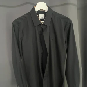 Svart Burberry Skjorta - Säljer nu min burberry skjorta då den aldrig riktigt kommit till användning. Har endast testats på och tagsen är tyvärr avklippta men finns separat som det syns på bilden. Hör gärna av er vid frågor eller om ni vill ha mer bilder👍