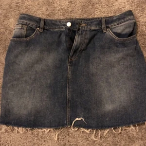 Jeanskjol med fransig kant - Mörkblå jeanskjol med rå, fransig nederkant och klassiska fickor både fram och bak. Storlek 42 men mer som en 40 