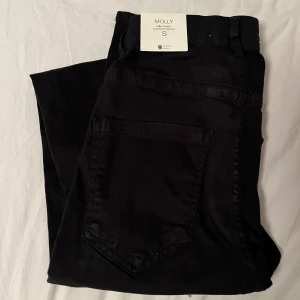 Svarta Molly jeansbyxor från Gina Tricot - Svarta Molly jeansbyxor från Gina Tricot med hög midja och skinny passform. Byxorna har klassiska bakfickor och är tillverkade i stretchigt material för en bekväm känsla. Perfekta till både vardags- och snyggare outfits. Helt oanvända och nya!