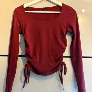 Vinröd ribbad topp - Vinröd långärmad topp från SHEIN med ribbad struktur och knyt i sidorna. Toppen har rund halsringning och är croppad.