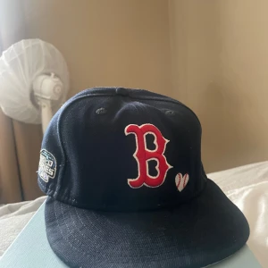 Mörkblå Boston Red Sox keps 59FIFTY - Säljer en mörkblå Boston Red Sox keps från New Era 59FIFTY-kollektionen. Kepsen har röd-vit broderad B-logga framtill, World Series-märke på sidan och texten 'Love & Hustle Game' broderad bak. Platt skärm och klassisk passform.