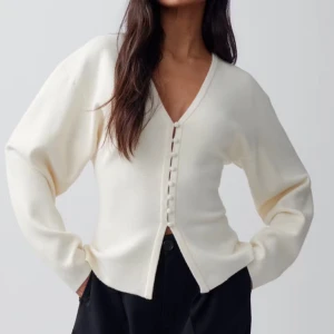 Vit kofta med knappar från Gina Tricot - Säljer en stilren vit kofta från Gina Tricot med v-ringning och dekorativa knappar framtill. Koftan har lång ärm och är tillverkad i ett mjukt material som passar perfekt till många olika outfits.