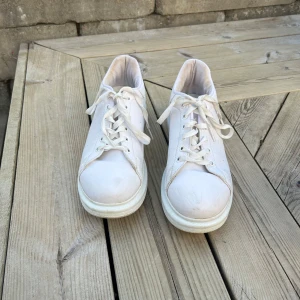 Vita sneakers med snörning - Klassiska vita sneakers med rund tå och platt sula. Skorna har snörning framtill och är tillverkade i syntetmaterial. Perfekta för en clean och stilren look.