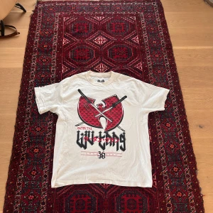 Wu-Tang Clan Tshirt - Säljer en vit t-shirt från Wu-Tang Clan med stort rött och svart tryck på bröstet. Klassisk passform med korta ärmar och rund hals. Perfekt för dig som gillar streetwear och hiphop.