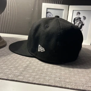 Svart New Era New York Yankees keps - Säljer en svart keps från New Era med New York Yankees-logga broderad framtill i vitt. Klassisk modell med platt skärm och MLB-logga baktill. Perfekt för dig som gillar sportig stil. änvänd 4 gånger 