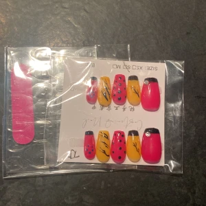 Färgglada lösnaglar med mönster - Säljer ett set lösnaglar i starka färger – röd, gul och svart. Naglarna har olika mönster som prickar och linjer. Medföljer gör en rosa nagelfil. Perfekt för dig som vill ha en unik och färgstark look.