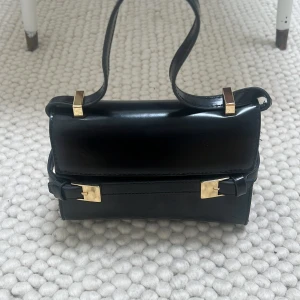 Svart mini väska - Svart liten väska från hm med guld detaljer, bra skick förutom några slitningar som kan visas närmare, långt band finns också