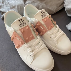 Valentino Rockstud Untitled sneakers med nitar - Säljer ett par vita Valentino Rockstud Untitled sneakers med ljusrosa band och ikoniska nitar. Skorna är INTE äkta och priset går att diskutera ☺️