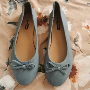 Ljusblå ballerinaskor med rosett - Säljer ett par ljusblå ballerinaskor från din sko. Skorna har en söt rosett framtill och rund tå. Perfekta för dig som gillar en enkel och stilren look. Passar till många olika outfits!