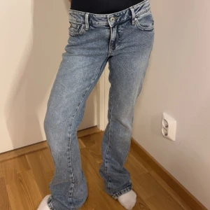 Lågmidjade Ljusblå bootcut jeans med broderad bakficka - Säljer ett par ljusblå jeans med bootcut passform och snygg broderad detalj på bakfickan. Jeansen har klassisk femficksdesign, normalhög midja och stängs med dragkedja och knapp. Perfekta till vardags för en avslappnad look.