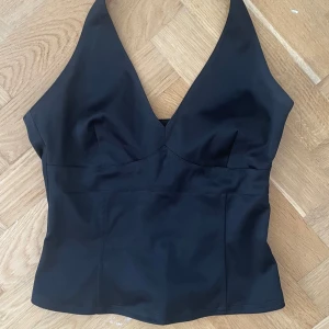 Svart halterneck topp - Säljer en svart halterneck top med en ”korsett” liknande passform och en dragkedja som knäpps i sidan. Den är knappast använd och har inga defekter. Hör av dig vid intresse! 🌺